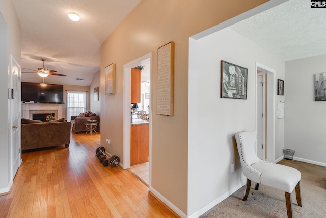 corridor with a textured ceiling, light wood-type flooring, visible vents, and baseboards