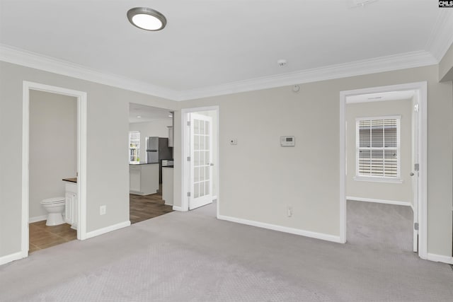 unfurnished bedroom featuring light colored carpet, ornamental molding, freestanding refrigerator, connected bathroom, and baseboards