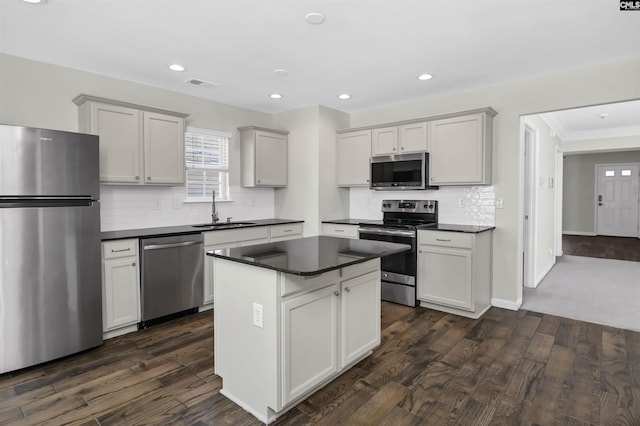 kitchen featuring dark wood finished floors, stainless steel appliances, dark countertops, a sink, and a kitchen island