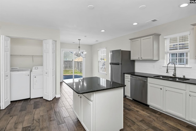 kitchen featuring stainless steel appliances, a kitchen island, a sink, washer and clothes dryer, and dark wood finished floors