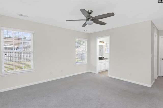 unfurnished bedroom featuring ceiling fan, connected bathroom, light colored carpet, visible vents, and baseboards