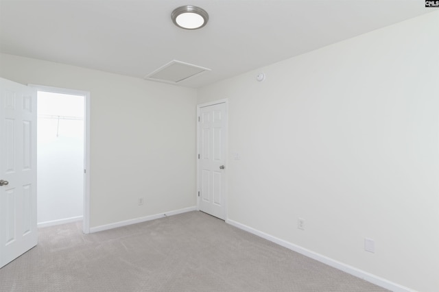 spare room with attic access, light colored carpet, and baseboards