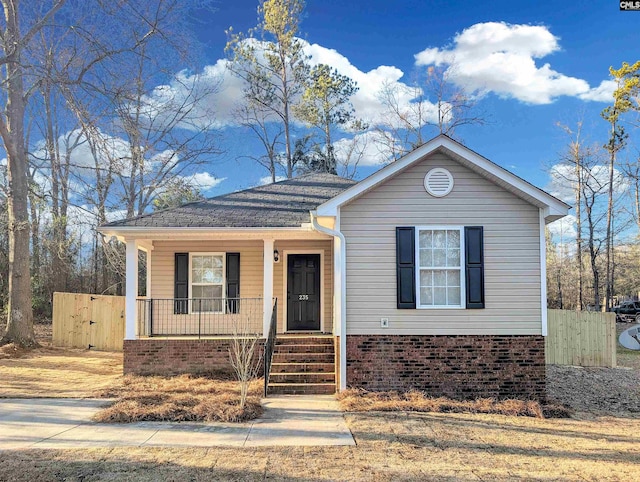 view of front of house with covered porch, brick siding, fence, roof with shingles, and a gate