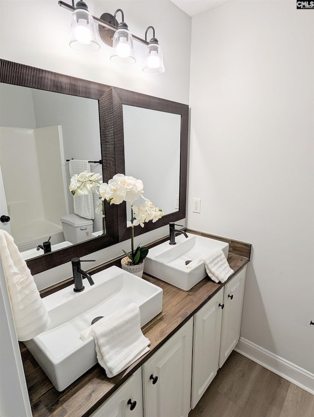 full bath featuring double vanity, toilet, a sink, wood finished floors, and baseboards