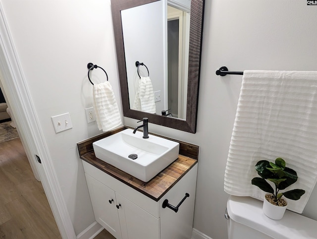 half bath featuring baseboards, vanity, toilet, and wood finished floors