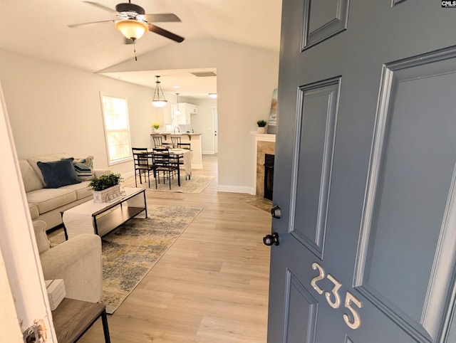 living area with ceiling fan, light wood-style flooring, a fireplace with flush hearth, baseboards, and vaulted ceiling