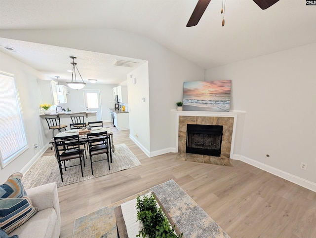 dining room featuring visible vents, light wood-style flooring, a tiled fireplace, vaulted ceiling, and baseboards