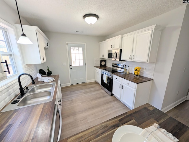 kitchen with light wood finished floors, white cabinetry, appliances with stainless steel finishes, and decorative light fixtures