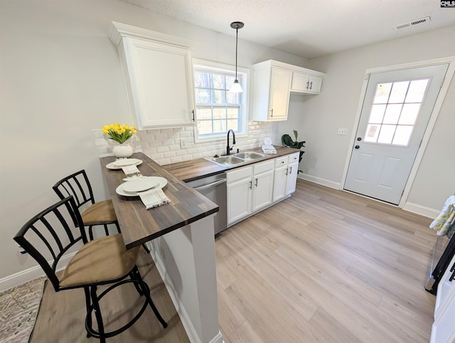 kitchen featuring visible vents, dishwasher, butcher block countertops, decorative light fixtures, and white cabinetry