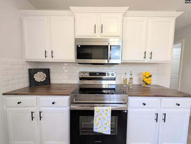 kitchen featuring a textured ceiling, stainless steel appliances, butcher block counters, white cabinets, and tasteful backsplash