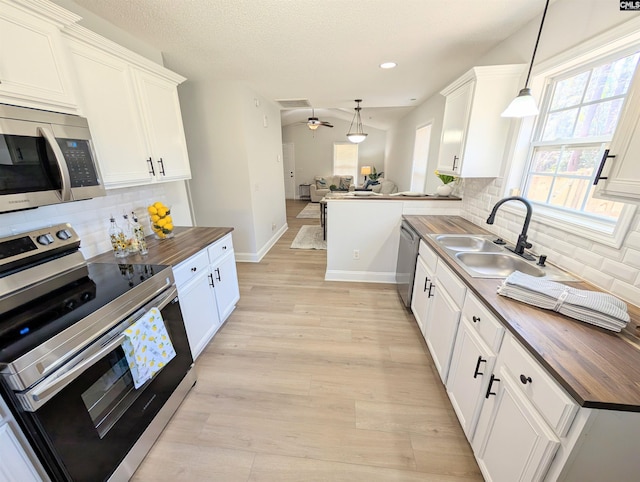 kitchen with appliances with stainless steel finishes, open floor plan, a sink, butcher block countertops, and a peninsula