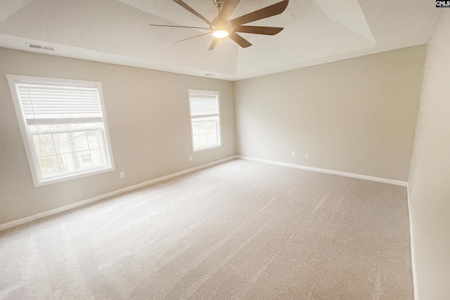 empty room featuring ceiling fan, light carpet, visible vents, baseboards, and a raised ceiling