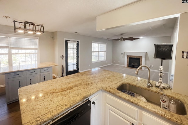 kitchen with light stone counters, a ceiling fan, open floor plan, black dishwasher, and a tiled fireplace