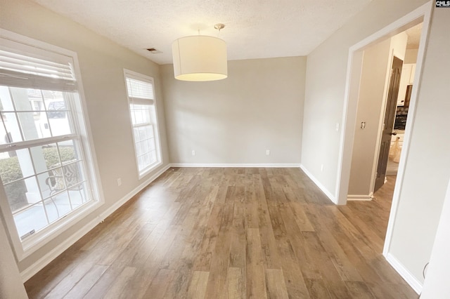 unfurnished room featuring visible vents, a textured ceiling, baseboards, and wood finished floors