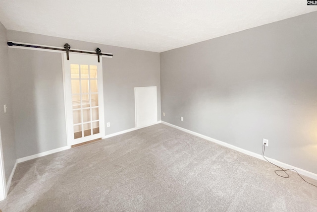 carpeted spare room with baseboards and a barn door