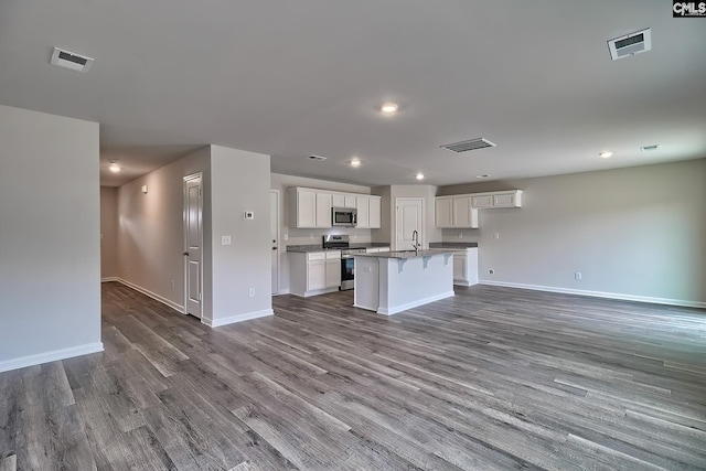 kitchen with appliances with stainless steel finishes, open floor plan, white cabinets, an island with sink, and a kitchen breakfast bar