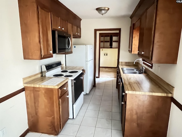 kitchen featuring light tile patterned floors, white appliances, a sink, light countertops, and brown cabinets