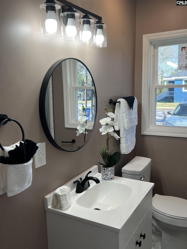 half bath featuring a wealth of natural light, vanity, and toilet