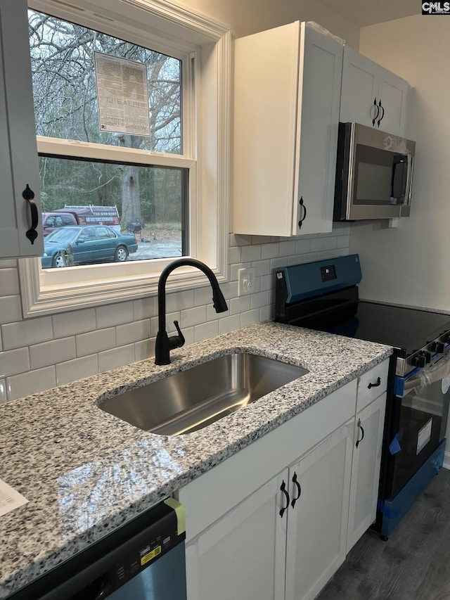 kitchen featuring appliances with stainless steel finishes, white cabinets, a sink, and light stone countertops