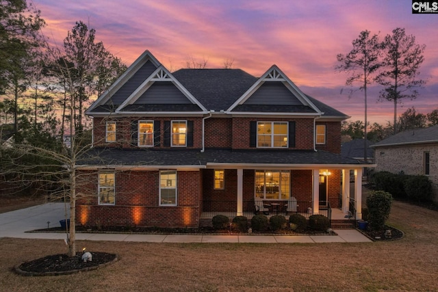 view of front facade with covered porch, brick siding, and a front lawn