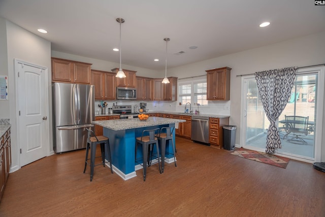 kitchen featuring light stone counters, a kitchen breakfast bar, hanging light fixtures, appliances with stainless steel finishes, and a center island