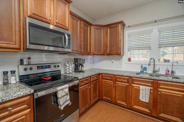 kitchen with brown cabinetry, appliances with stainless steel finishes, light stone counters, a sink, and backsplash