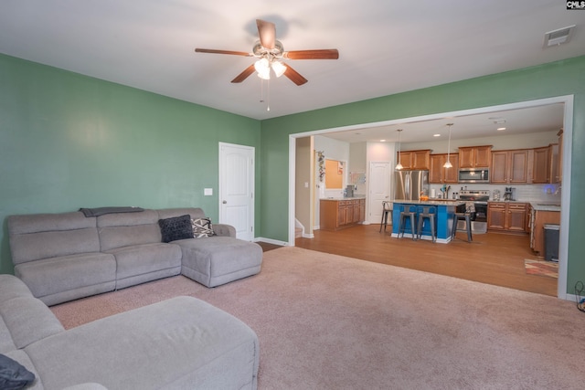 living area featuring a ceiling fan, light colored carpet, visible vents, and baseboards