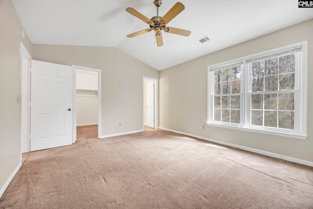 unfurnished bedroom featuring a walk in closet, visible vents, light carpet, vaulted ceiling, and baseboards