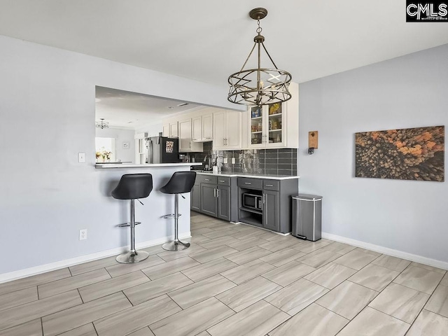 kitchen featuring a breakfast bar, gray cabinets, light countertops, freestanding refrigerator, and white cabinetry