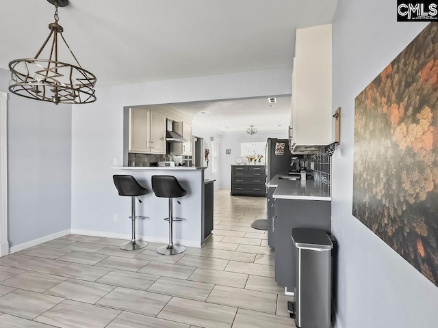 kitchen featuring wall chimney exhaust hood, light countertops, backsplash, a sink, and a kitchen breakfast bar