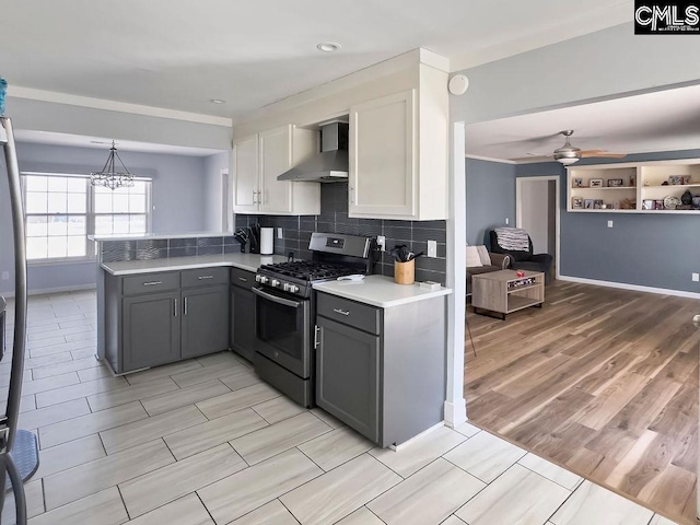 kitchen featuring white cabinetry, light countertops, gray cabinets, wall chimney exhaust hood, and gas range