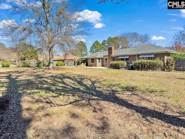 view of front facade with brick siding, a chimney, a front lawn, and fence