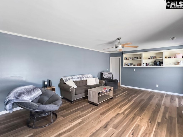 living area featuring baseboards, visible vents, a ceiling fan, ornamental molding, and wood finished floors