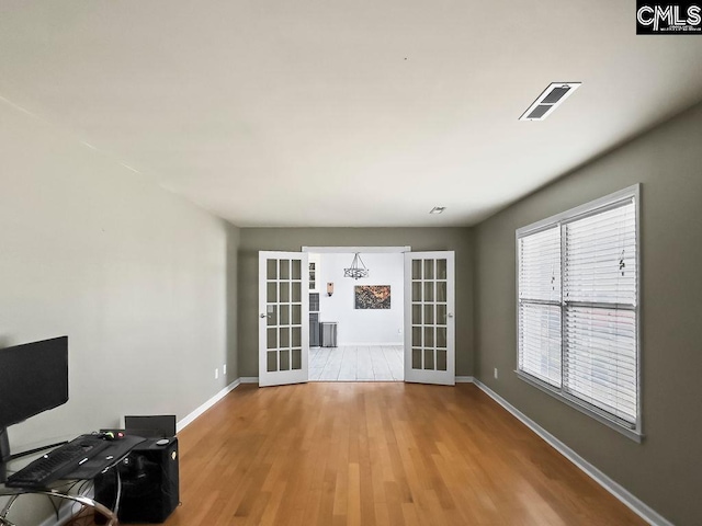 unfurnished living room with french doors, visible vents, baseboards, and wood finished floors