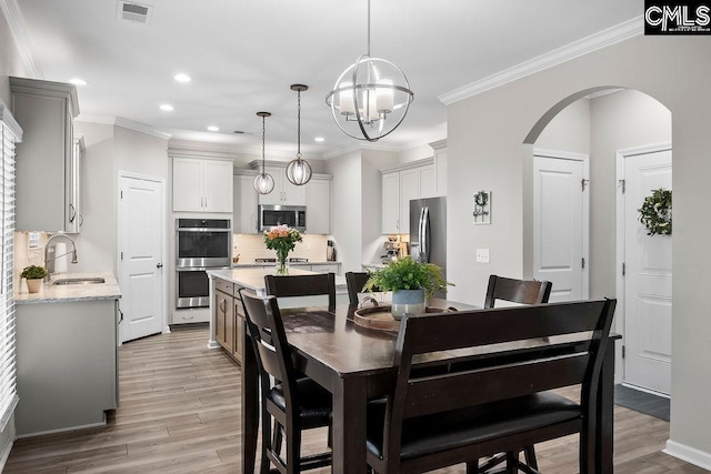 dining space featuring light wood-type flooring, arched walkways, visible vents, and crown molding