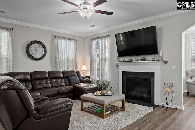 living area with arched walkways, ornamental molding, wood finished floors, and visible vents