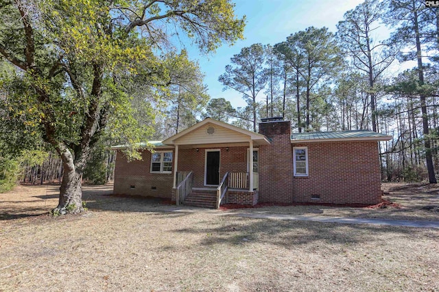 view of front of house featuring metal roof, covered porch, brick siding, crawl space, and a chimney