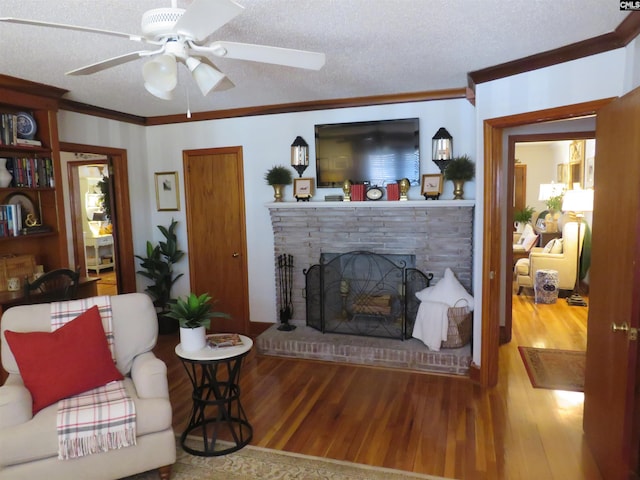 living area featuring ornamental molding, a brick fireplace, ceiling fan, a textured ceiling, and wood finished floors