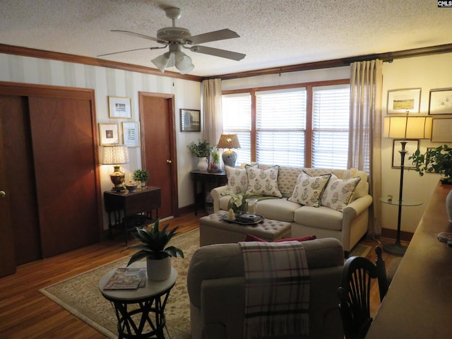 living room featuring ceiling fan, ornamental molding, a textured ceiling, and wood finished floors