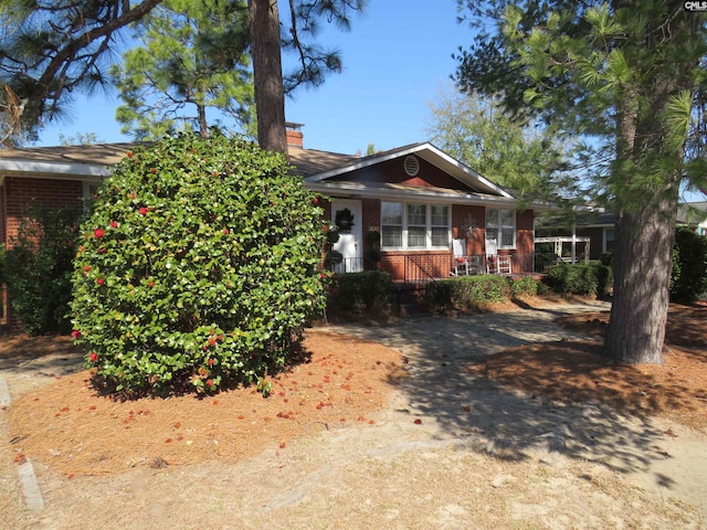 view of front of house featuring a chimney, a porch, and brick siding