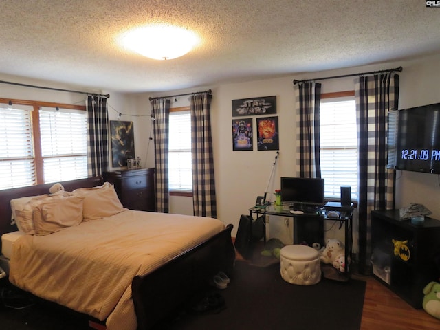 bedroom with a textured ceiling, multiple windows, and wood finished floors