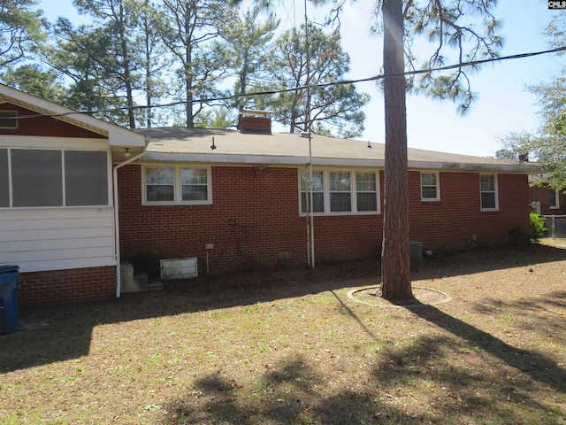 view of property exterior featuring a sunroom, brick siding, a yard, and a chimney