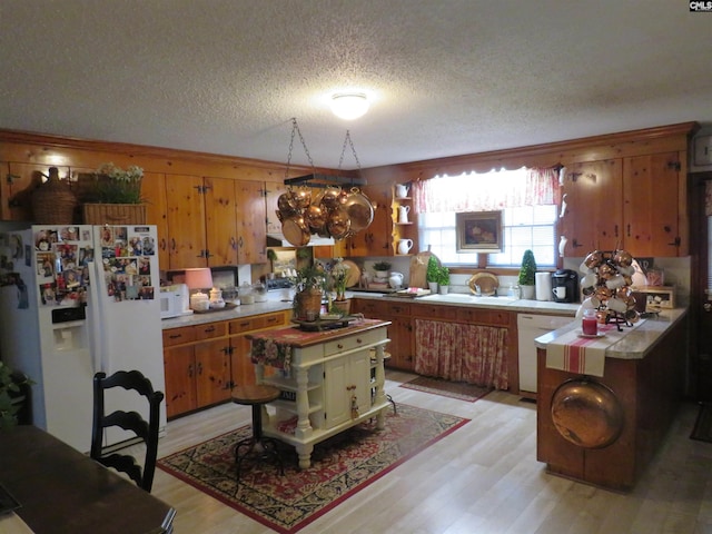 kitchen with white appliances, a sink, light wood-style flooring, and brown cabinets