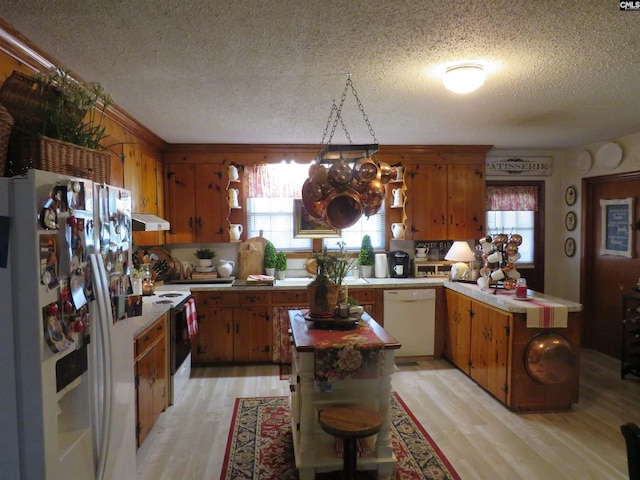 kitchen featuring white appliances, brown cabinetry, light wood-style flooring, a kitchen island, and light countertops