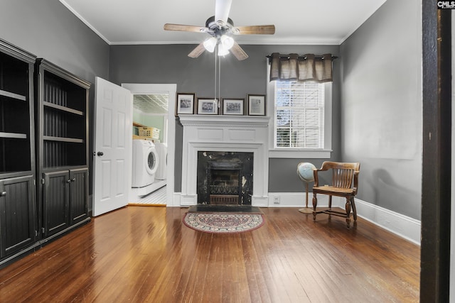 sitting room with hardwood / wood-style flooring, a premium fireplace, a ceiling fan, baseboards, and crown molding