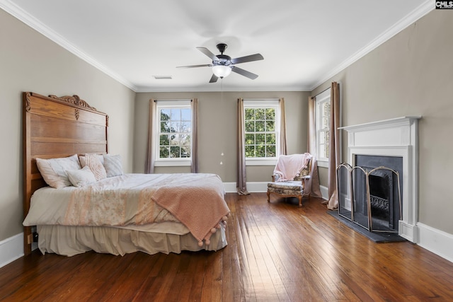 bedroom with a fireplace with raised hearth, visible vents, baseboards, dark wood finished floors, and crown molding