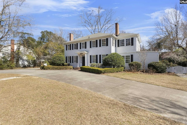 colonial-style house with driveway, a chimney, fence, and a front yard