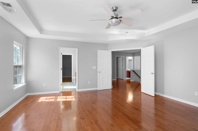 empty room with a raised ceiling, visible vents, dark wood finished floors, and baseboards