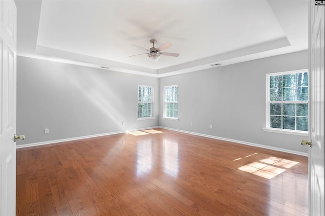 empty room with baseboards, a raised ceiling, and wood finished floors