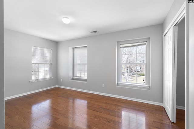 unfurnished bedroom with dark wood-type flooring, multiple windows, visible vents, and baseboards